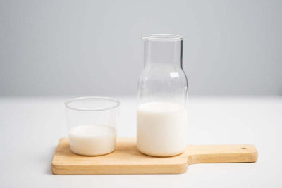 Un vaso de cristal con leche junto a una botella de cristal con leche